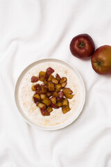 A warm bowl of oatmeal topped with caramelized apples, perfect for a cozy breakfast on white fabric background.