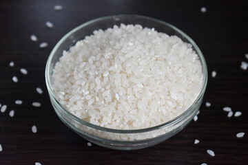 Plate with rice side view. Rice porridge in glass bowl isolated on black background with scattered rice grains on table, side view