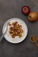 A warm bowl of oatmeal topped with caramelized apples, perfect for a cozy breakfast on dark background.