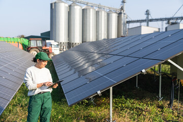 Female farmer with digital tablet on a modern farm using solar panels. Agricultural silos in the...
