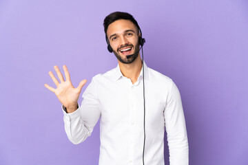 Telemarketer man working with a headset isolated on purple background counting five with fingers