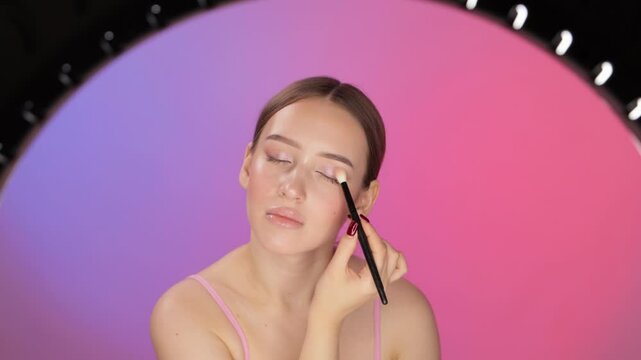 Beautiful green-eyed girl blogger does  makeup in the studio. She teaches subscribers makeup. Professional makeup and cosmetic skin care.