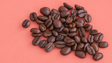 Pile of roasted coffee beans on a pink background. Ideal for concepts of coffee culture, fresh brew, caffeine, and the artisanal coffee industry.
