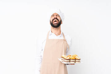 Young man holding muffin cake over isolated white background shouting to the front with mouth wide open