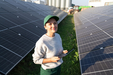 Female farmer with digital tablet on a modern farm using solar panels. Agricultural silos in the...