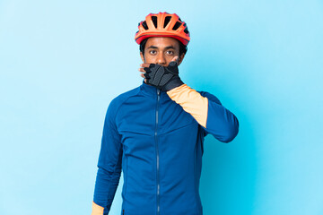 Young cyclist man with braids over isolated background covering mouth with hand