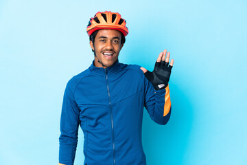 Young cyclist man with braids over isolated background saluting with hand with happy expression