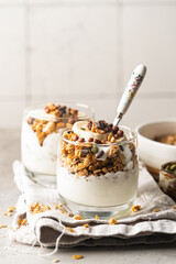 Crunchy granola with yogurt, banana, nuts, chocolate and honey in a glass on white background. Healthy breakfast concept.