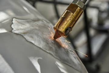 A close-up of a welding process, showing a brass welding torch creating sparks on a metallic...