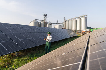 Female farmer with digital tablet on a modern farm using solar panels. Agricultural silos in the...