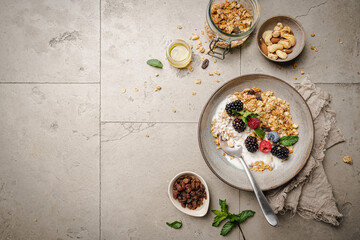 Bowl of homemade granola with yogurt and fresh berries on gray background from top view