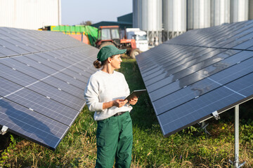 Female farmer with digital tablet on a modern farm using solar panels. Agricultural silos in the...