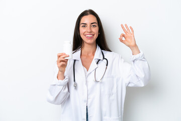 Young caucasian woman isolated on white background wearing a doctor gown and holding pills