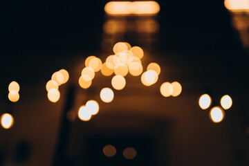 Fototapeta premium Decorative string lights at night time, Defocused Background, night city backdrop, party time with Yellow bokeh balls. Abstract blurred warm light