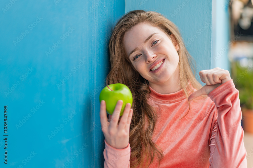 Poster Young redhead woman with an apple at outdoors proud and self-satisfied