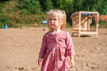 Caucasian little child girl two-year-old in dress on a sea beach in summer, sstkbabies. Family vacation, cold season.