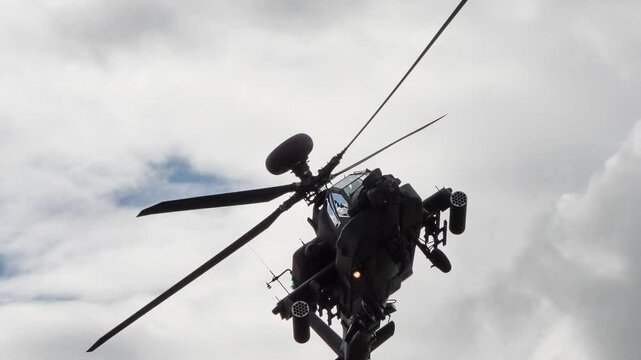 close-up of British army Boeing Apache Attack helicopter longbow gunship AH2 AH64E AH-64E ArmyAirCorp banking hard right and flying directly overhead in low level flight