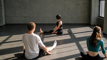 Gymnastic class. Yoga exercise. Female sport instructor training group people body stretch workout gymnastic practice on mat in gym fitness studio indoors.