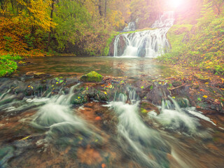 wide angle view to waterfall and river with sun spot in autumn forest