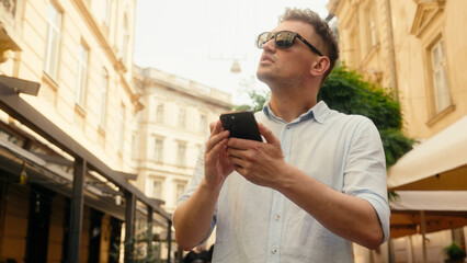 Man in sunglasses male tourist traveler customer businessman Caucasian guy walking searching address location in city using mobile phone online map gps navigator looking direction guide travel outdoor