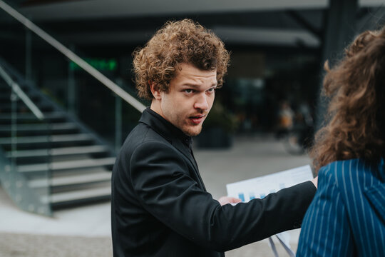 Businessman discussing a sales report with a colleague outside a modern office building. Engaged in conversation and analysis.