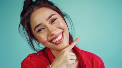 Fototapeta premium A woman with a bright red shirt smiles and points to her mouth, conveying a sense of amusement or secrecy
