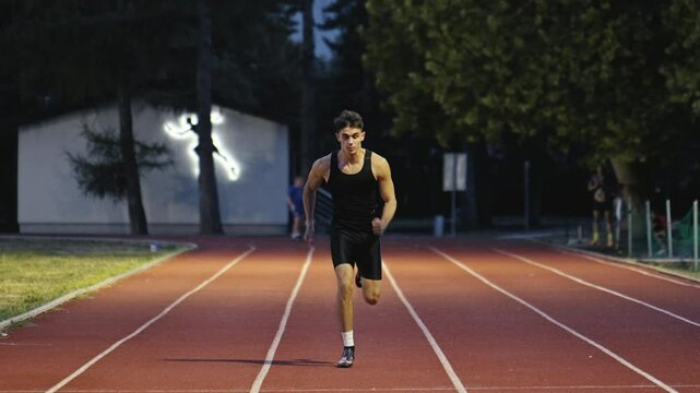 Vertical video of a young athlete running on an athletics track on a sunny morning along a lane of the track. Concept of sport and perseverance.