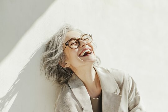 A woman with glasses smiles while leaning against a wall, suitable for use in various social media posts or personal blogs