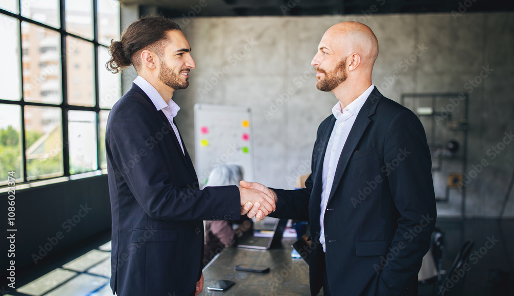 Poster two men in suits greet each other with a handshake in a contemporary office. a group of colleagues i