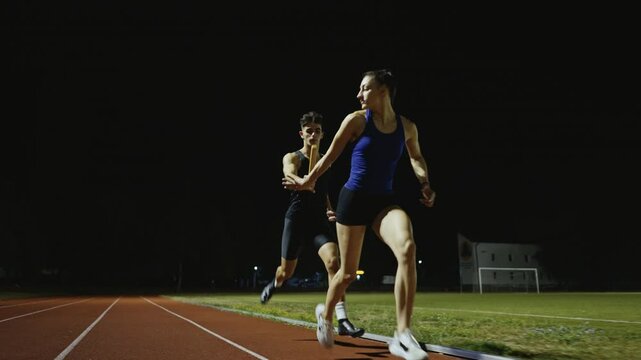 Athletes couple, male and female running a relay race and pass the baton on the athletics race track