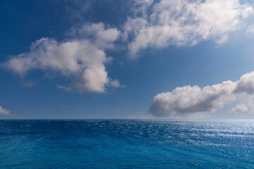 Fototapeta premium Seascape with blue sea over blue sky with white clouds with sun reflections. Seen panorama over Mediterranean sea seen from Corsica Island, France