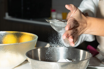 Close-up of female hand sifting flour into bowl for baking preparation. Stage of cooking pie.