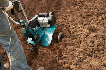 A dacha farmer at the controls of a compact motorized cultivator. Spring soil preparation on the...