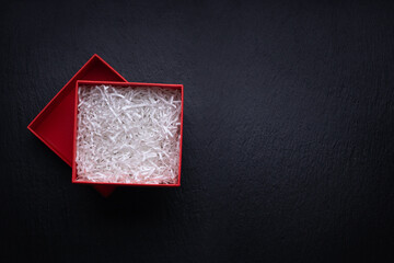 Top view of red box for  gift filled with decorative shredded white paper on black background