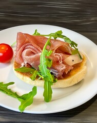Sandwich with jamon and arugula on background cherry tomato on white plate. sandwich