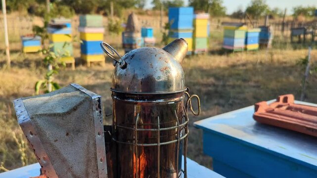 A smoker tool used for fumigating beehives to help with honey extraction, placed against the backdrop of a beekeeping farm.