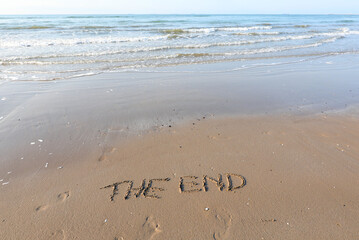 text THE END are written in the sand on a beach and an ocean wave is about to erase them