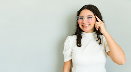 Portrait of a happy and bright teenage girl in glasses, pointing to her new pair of glasses in a studio