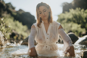 Serene woman in a flowing white dress enjoying the tranquil river setting, surrounded by nature. Peaceful and calm moment in the lush greenery.