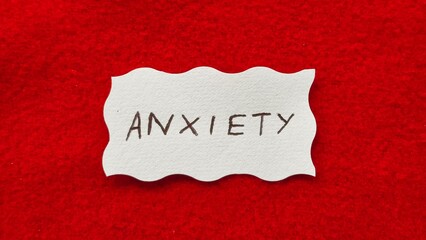 Anxiety word letters text handwritten calligraphy design on white paper label note isolated on a red background surface with copy space. Closeup macro top view. Anxiety creative concept.