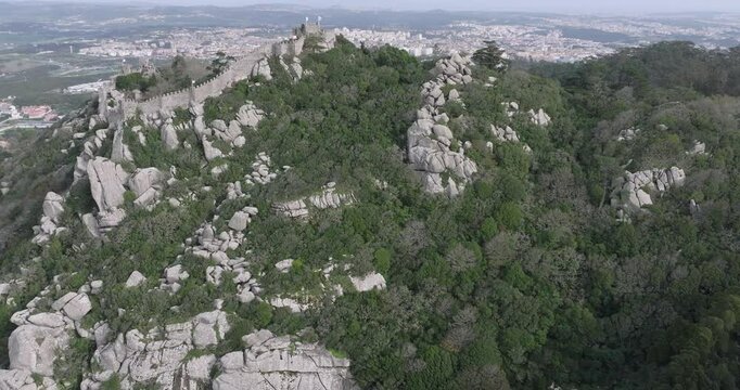 Aerial drone shot of the Castle of the Moors, Castelo dos Mouros, hilltop medieval castle in Sintra, Portugal, Europe. Overcast with clouds. Shot in 5K ProRes 422 Log