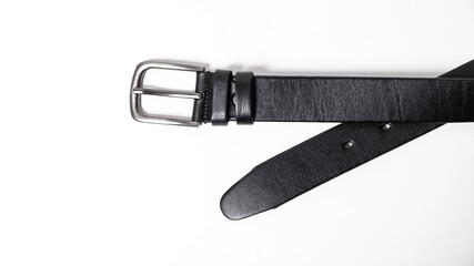 Black Classical leather Belt isolated on white background close-up. Fashionable unisex accessory with dark chrome matted metal buckle. Man lux strap. Haberdashery goods. Minimalistic style. Cross X