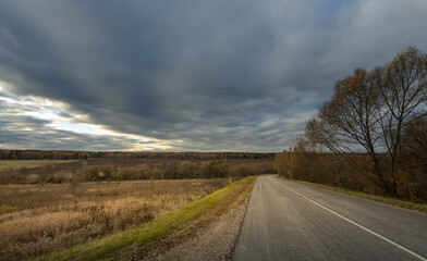 A road with a tree in the background and a cloudy sky