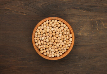Chickpeas filling a wooden bowl on a dark wooden table