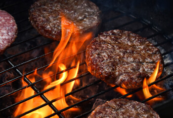 Delicious hamburgers grilling on barbecue with flames