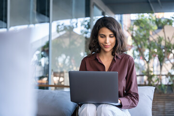 Beautiful middle eastern indian female freelancer working remotely on business project. Young latin, arabian freelance woman student worker using laptop for study sitting outdoors at cafe. Copy space