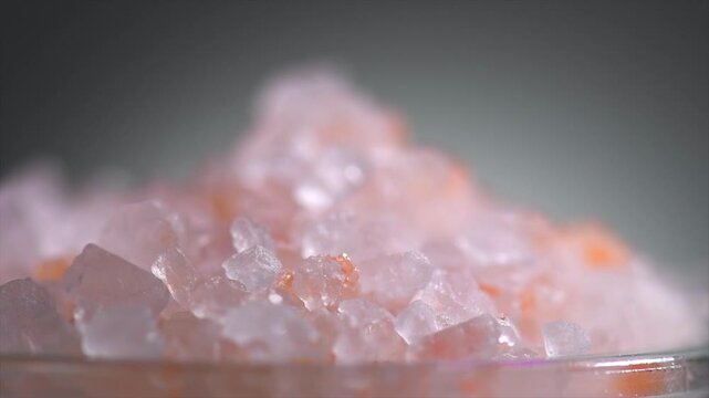 Himalayan salt, pink Himalayan salt crystals close up. Pink coarse salt crystals macro shot, rotating over gray background, slow motion video