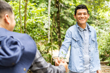 Latino man smiling as he is handing a small plant to another person in the background. Concept of...