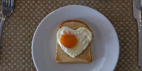 Heart shaped egg in toasted slice of rye bread on white ceramic plate. St Valentine's day concept. 