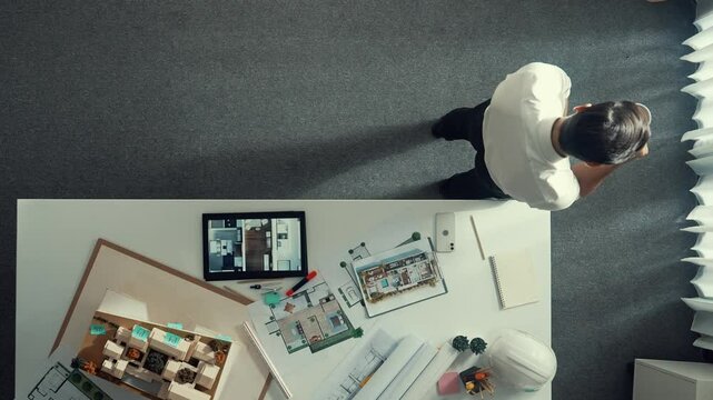 Top view of engineer drink coffee and thinking about house plan at meeting table with equipment and safety helmet scatter around. Aerial view of stressful manager walking and standing. Alimentation.